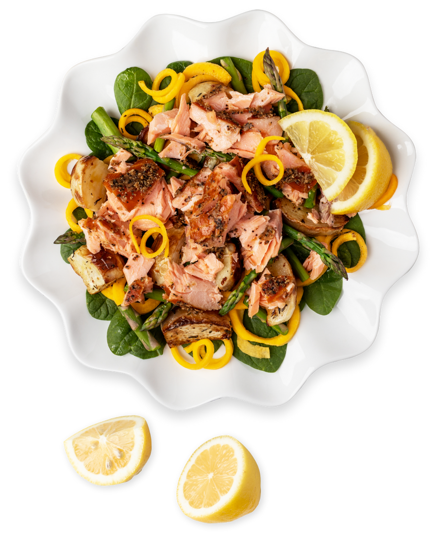 Salmon pasta spinach dish in a white serving plate with lemons